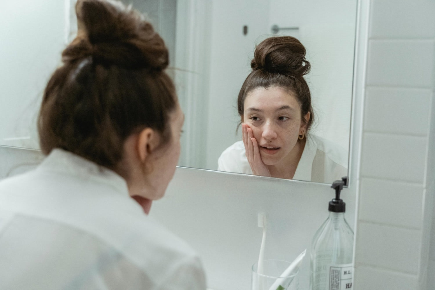 Woman touching her skin in front of a mirror during a humid morning skincare routine